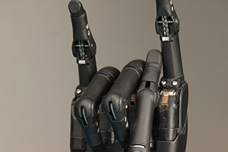 Photo of a mechanical hand making the Hookem Horns sign.
